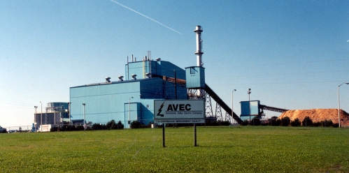 Sign that says AVEC in foreground and an industrial plant in the background.